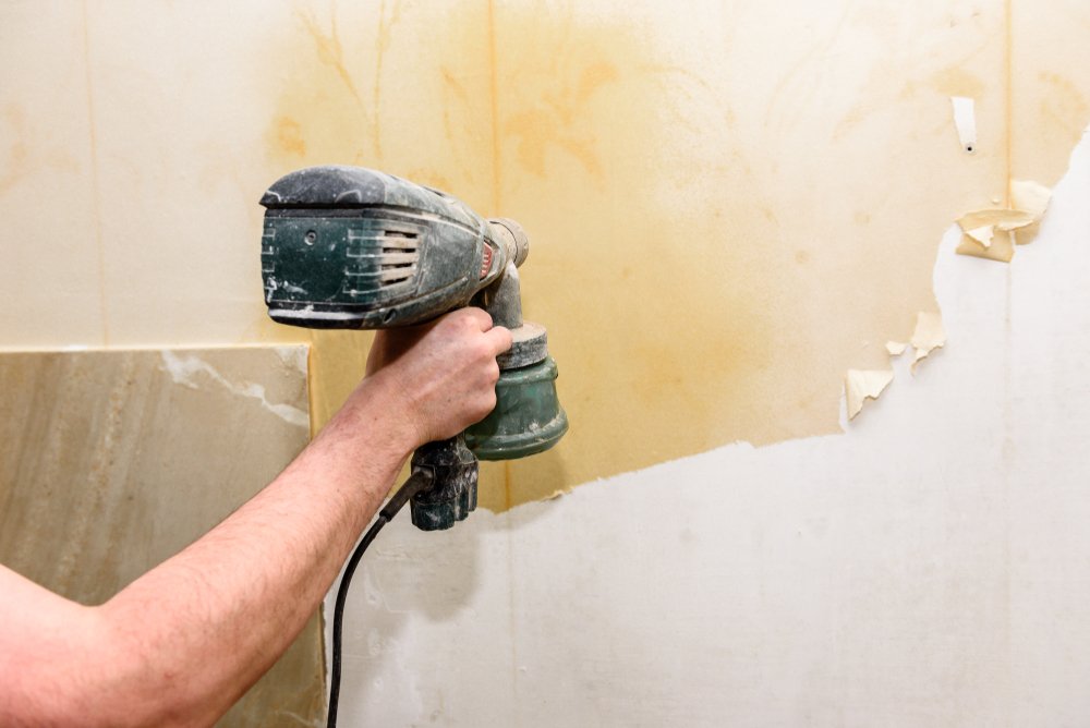 Een persoon brengt behangverwijderaar aan op een muur met behulp van een spons, om het behang gemakkelijk van de muur te verwijderen.