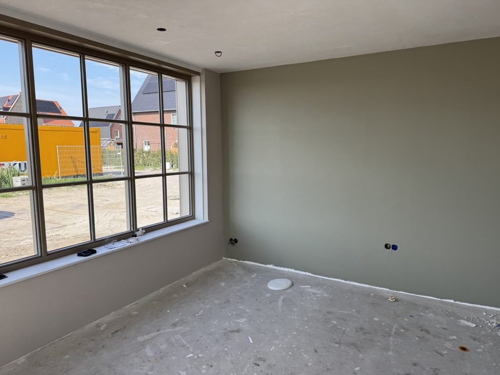 Kamer met een egaal afgewerkte wand in een grijsgroene tint en een groot raam