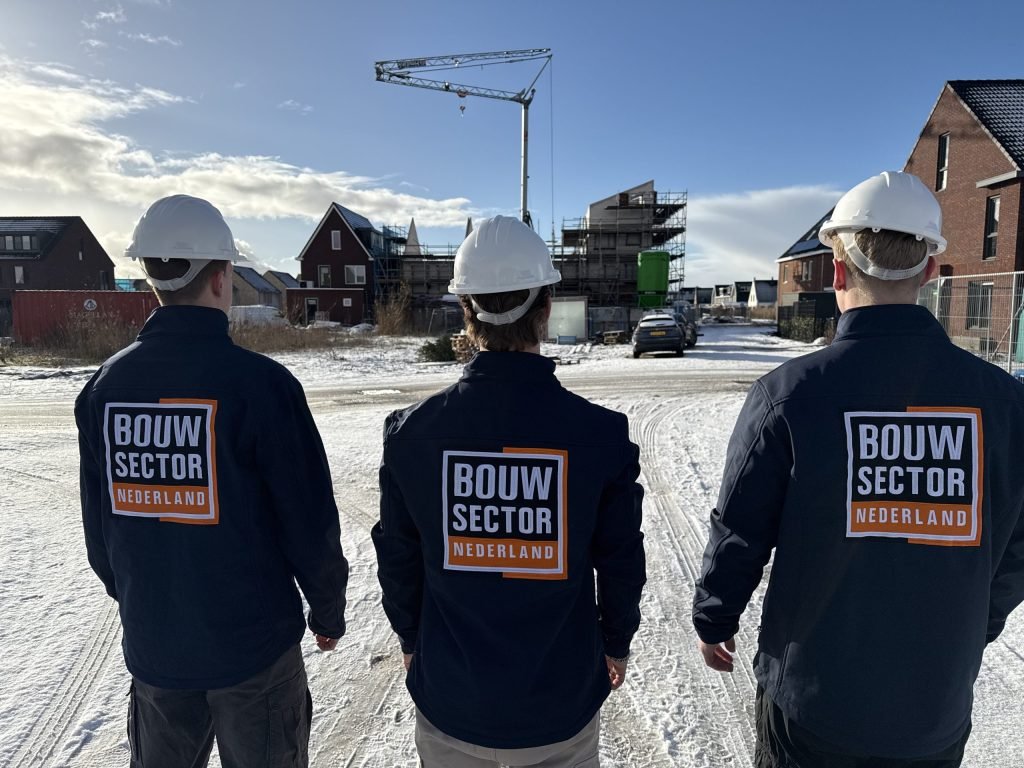 Drie collega's in werkkleding met het logo van Bouwsector Nederland overzien een bouwplaats met steigers